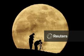 A couple and their daughter use a telescope to observe the last supermoon of 2025, known as the Cold Moon, in Aguimes