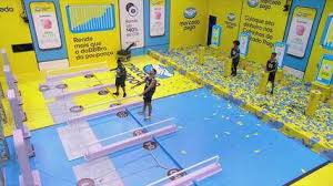 Participantes em prova de resistência no BBB 23, com cenário amarelo e azul e confetes espalhados.