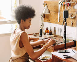person crafting handmade jewelry at a workbench resmi