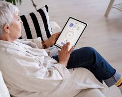 Изображение: elderly person wearing a discreet health monitoring device, with data displayed on a caregiver's smartphone