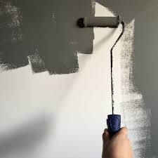 a hand holding a paint roller and painting the wall gray