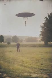 This is a black-and-white, surreal image depicting an alien abduction scene. A large UFO hovers in the night sky, emitting a beam of light downward. Within the beam, a human figure is