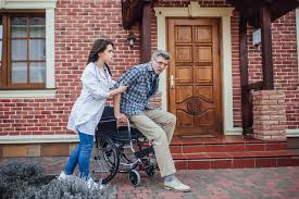 caregiver assisting a senior man in a wheelchair outside his home entrance