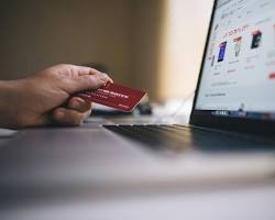 person holding a credit card in front of a laptop screen resmi