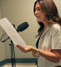 Atriz brasileira Carolina Dieckmann gravando áudio em estúdio com microfone profissional e roteiro em mãos.