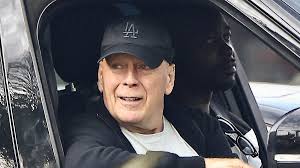 Bruce Willis smiles in rare sighting as he dons Dodgers cap on drive with 
bodyguard in LA amid aphasia and dem