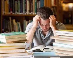 Image of student surrounded by textbooks and a calculator, looking stressed