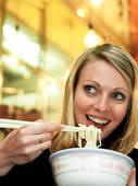 Woman eating noodles with chop sticks, smiling, low angle view. Fotosearch Stock ImagesRF Royalty Free - x19329110