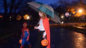 Halloween 2026 weather forecast scene with costumed children trick-or-treating under cloudy skies and porch lights