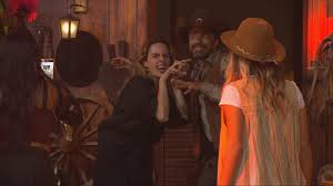 Pessoas fantasiadas em uma festa temática de velho oeste, com decoração rústica e iluminação dramática.