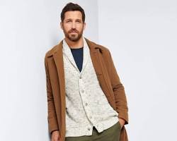 man layering a cardigan over a buttondown shirt and jeans