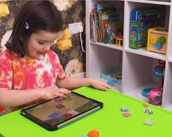 Изображение: child laughing while playing an interactive game on a tablet that teaches basic math and language skills