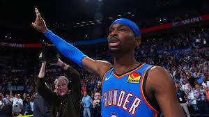 Jogador de basquete do Oklahoma City Thunder, Lu Dort, comemora com a torcida em quadra. Dort usa bandana azul e uniforme do…