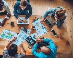 Image of group of people working together at a table with laptops and papers